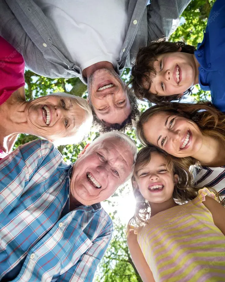 Healthier lives for people of every generation Smiling multigenerational family with heads together in a circle outdoors under green trees