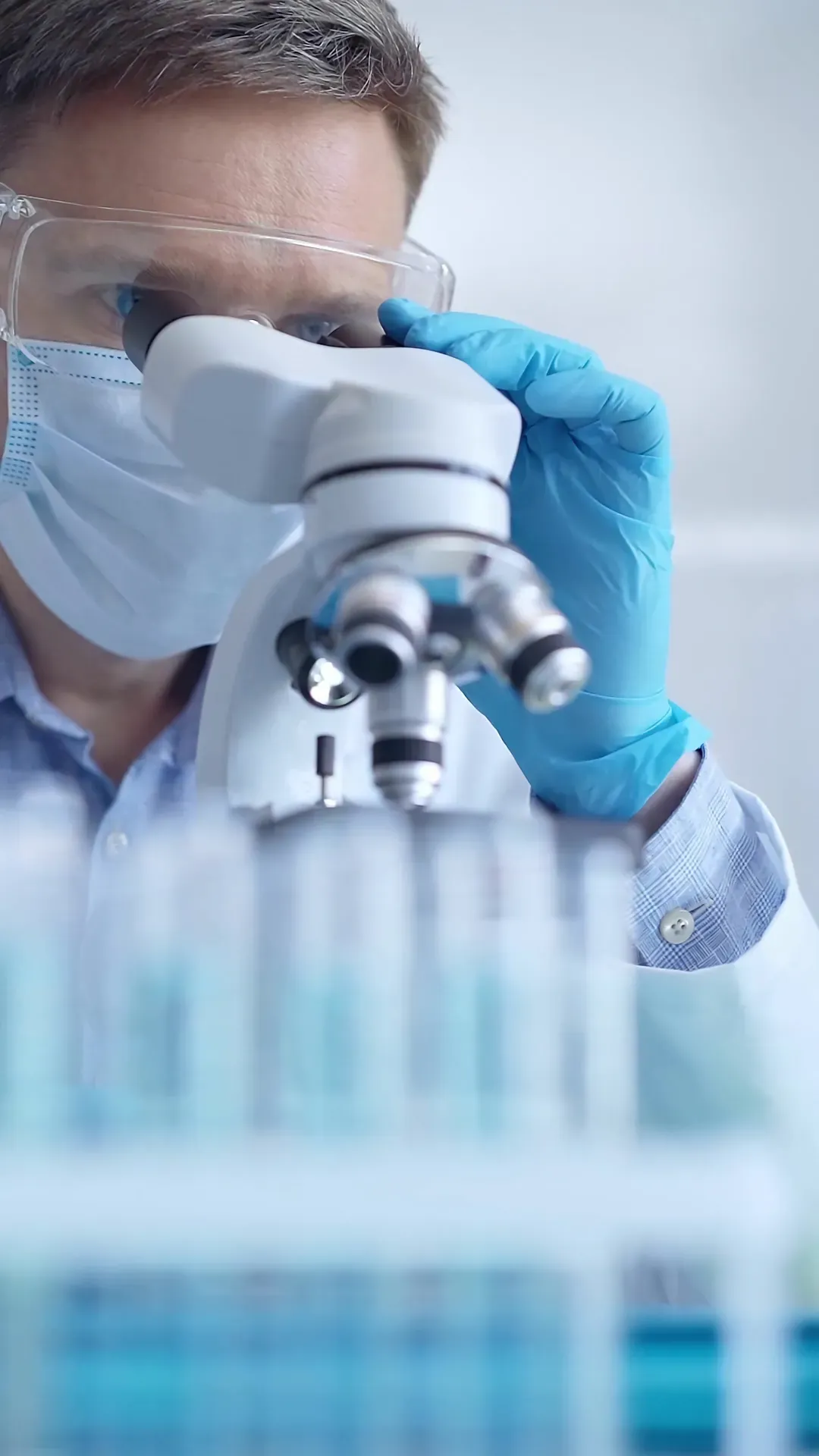 Biotechnology research under the microscope Scientist in safety glasses and blue gloves examining samples through a laboratory microscope